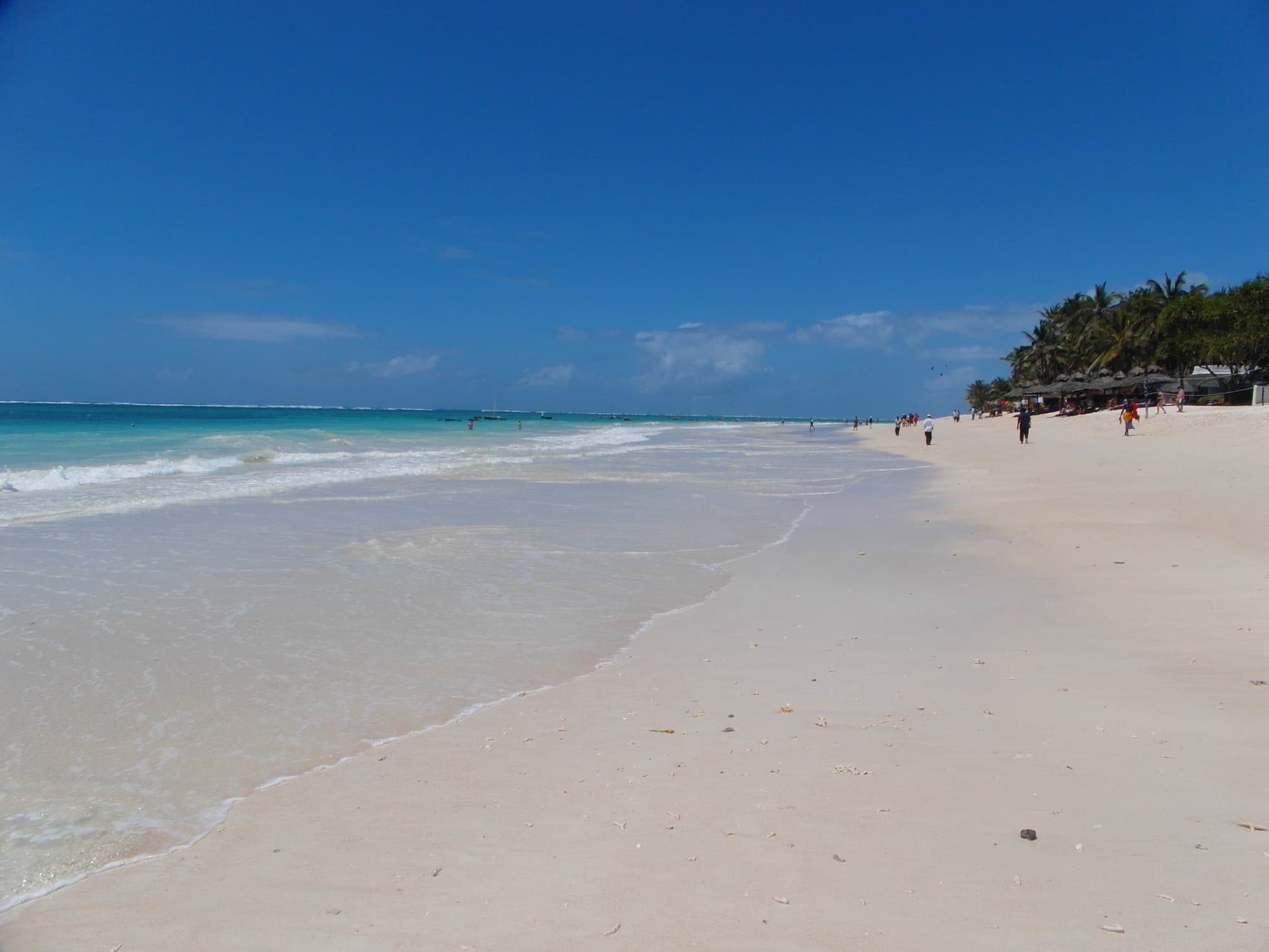 Lang wit zandstrand met turquoise water en palmen aan Diani Beach in Kenia